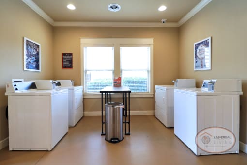 A laundry center with multiple washers and dryers with table and large windows.