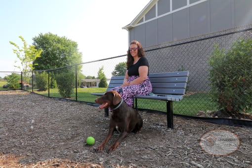 A woman sitting on a bench in the Bark Park with her dog.