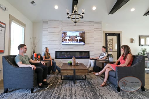 A group of people relaxing in arm chairs, watching TV and enjoying the fireplace in the clubhouse lounge.