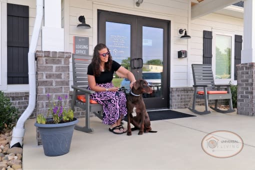 A woman sitting on a bench in front of the clubhouse with her dog.