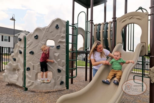 A mother and two children playing on a slide on a playground.