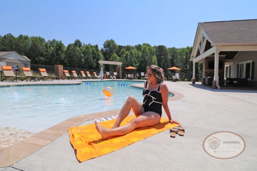 A woman sitting on a towel by a pool.