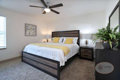 A bedroom with a bed, carpet, ceiling fan, and white walls.