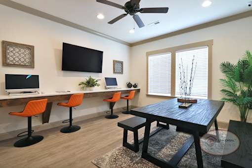 A business center with orange barstool seating, computers and free Wi-Fi, flat screen TV, large window, and table.
