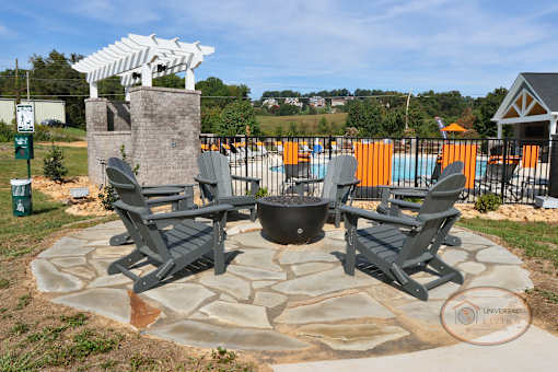 A firepit on a stone patio by the pool surrounded by Adirondack chairs.