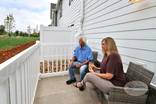 A man and woman sitting on a fenced in patio looking at the scenery.