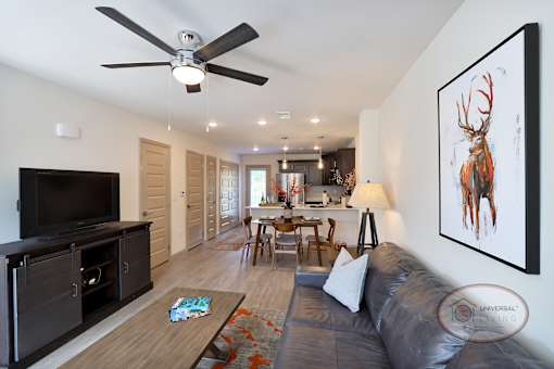 Another view of the furnished living area with hardwood vinyl flooring, white walls, with the kitchen and patio door visible in the background.