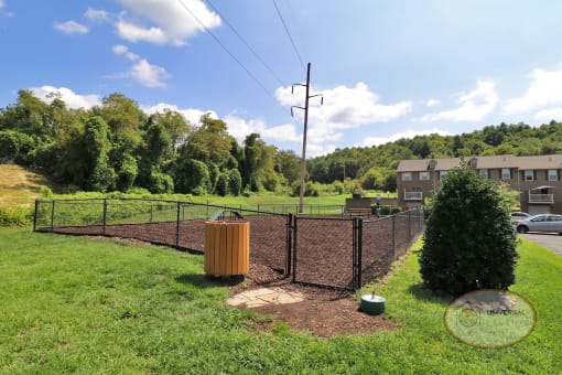 A fenced in dog park with a water fountain for pets and a bench.
