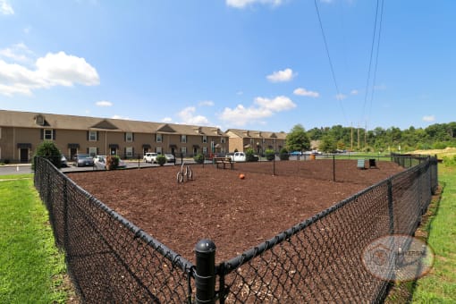 A fenced in dog park in front of an apartment building.
