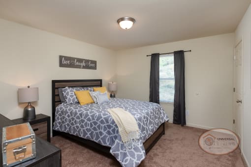 A bedroom with a large bed, carpet, white walls, and a large window.