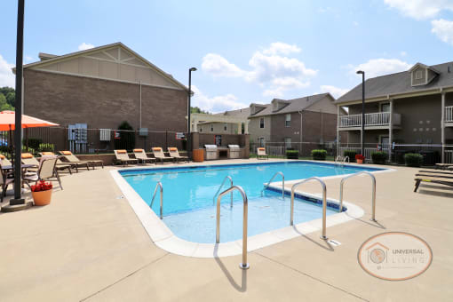 A pool with large sundeck, complete with lounge chairs and tables with umbrellas.