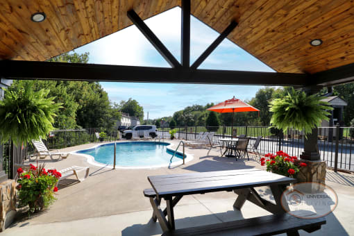 A covered picnic area next to a pool, surrounded by fresh flowers.