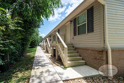 The front of a row of tan apartment buildings with a sidewalk leading to stairs.