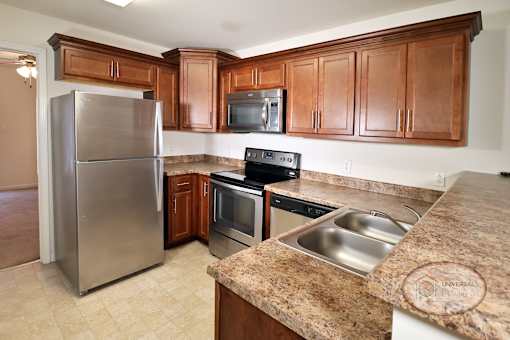A kitchen with solid surface countertops, dark wood cabinets, and stainless steel appliances.