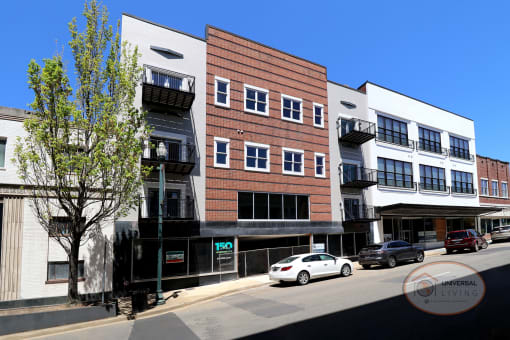 The front of a white and brick downtown apartment complex with balconies and large windows.