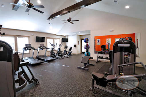 a gym with cardio equipment and ceiling fans