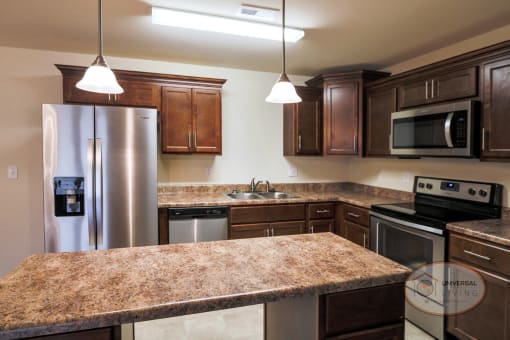 A kitchen with speckled countertops, dark cabinets, and stainless steel appliances.