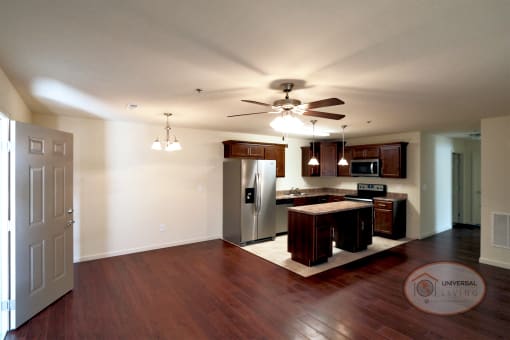 The interior of an empty apartment home with hardwood flooring and a kitchen with stainless steel appliances.