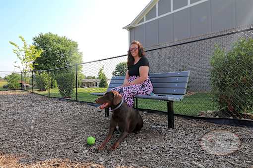 A woman sits on a bench in the Bark Park with her dog.
