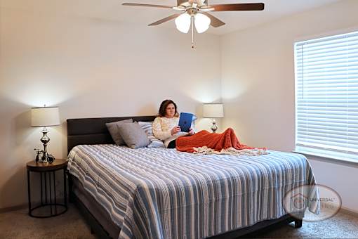 A woman is sitting on a bed looking on an IPad.