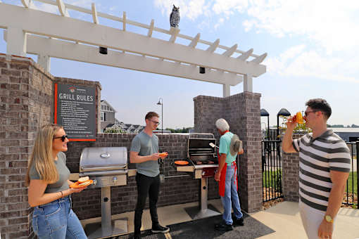 A group of people gathered around a man cooking burgers at the grill.