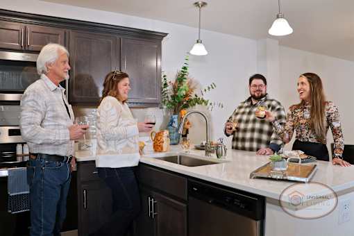 Four people standing in a kitchen, laughing and drinking.