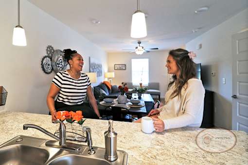 Two women are sitting at a kitchen counter laughing and drinking coffee.