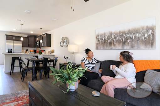 Two women are sitting on a couch in a living room talking and drinking coffee.