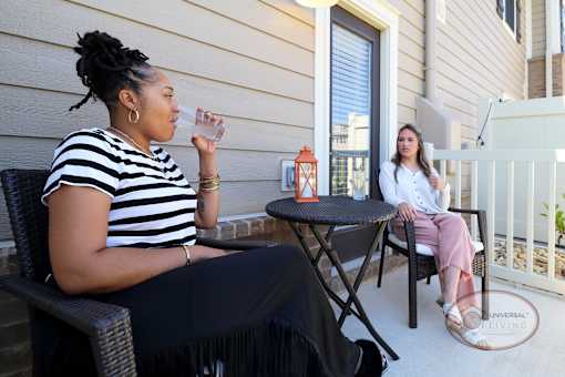 Two women sitting on a patio, one drinking from a glass.