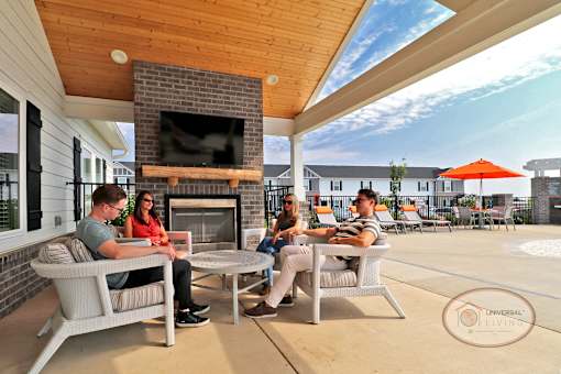 A group of people sitting around the clubhouse lounge with a flat screen TV and fireplace.
