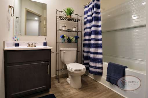 A bathroom with hardwood vinyl flooring, dark cabinets, and white countertops.