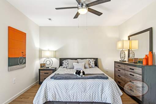 A bedroom with a hardwood vinyl flooring, dresser, and ceiling fan.