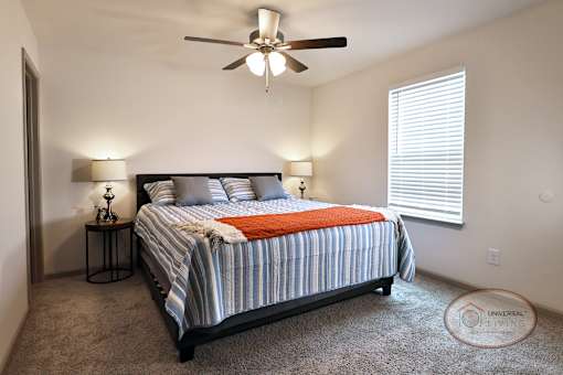 A bedroom with a queen size bed, carpet, and a ceiling fan.