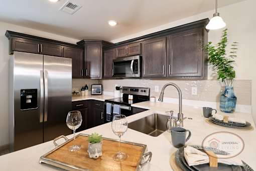A kitchen with dark cabinets, white countertops, and stainless steel applinaces.