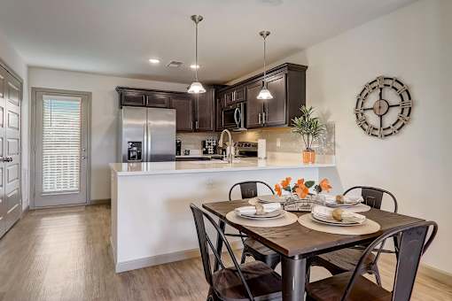 A kitchen with hardwood vinyl flooring, white walls, dark cabinets, and stainless steel appliances.