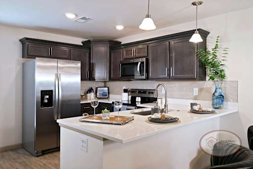 A kitchen with stainless steel appliances, white counters, and dark cabinets.
