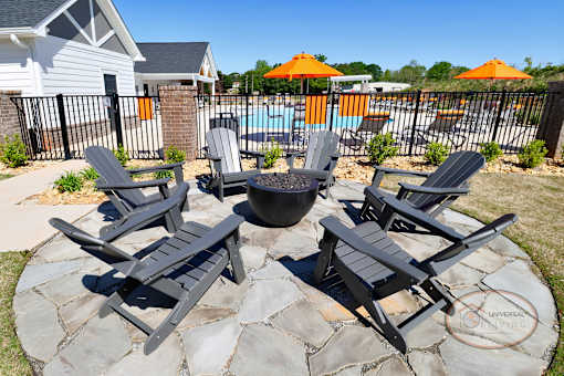 A set of four black Adirondack chairs are arranged around an outdoor fire pit.