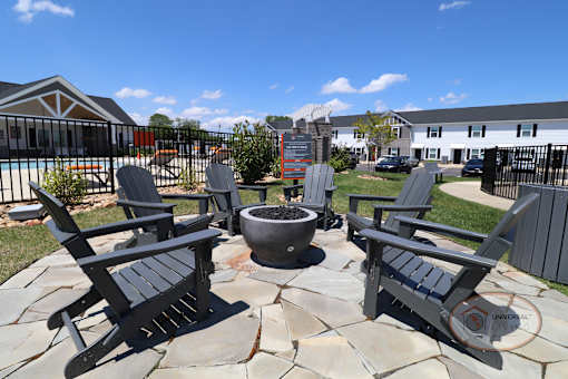 A fire pit surrounded by grey Adirondack chairs.