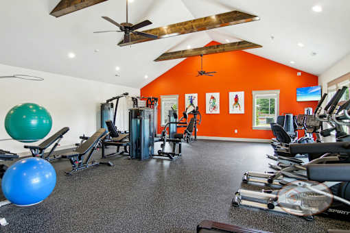A gym with flat screen TVs, weight training, and cardio equipment in front of an orange accent wall.