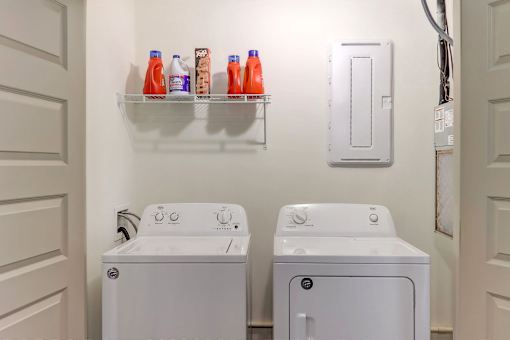A laundry room with a washer and dryer and a shelf with detergent.