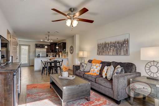 A living room with hardwood vinyl flooring, and a kitchen in the background with stainless steel appliances.
