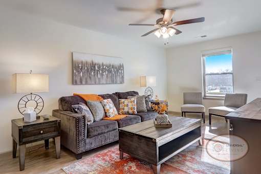 A furnished living room with a grey couch, window, and ceiling fan.