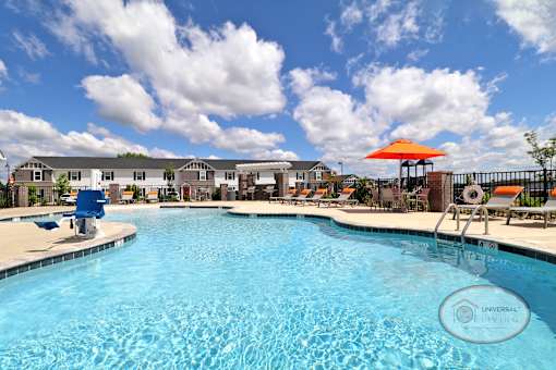 A swimming pool with a blue sky and rows of white and gray apartments in the background.
