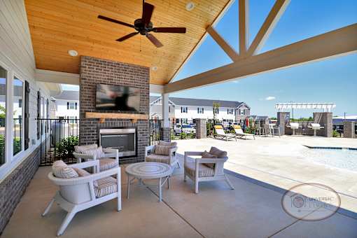 A covered poolside patio with flat screen TV, fireplace, ceiling fan, and lounge seating.