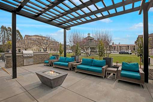 A patio with a fire pit and couches under a pergola.