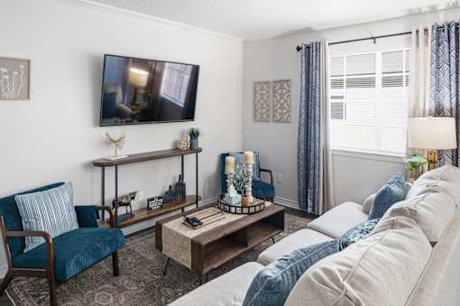 A living room with a blue chair, a white sofa, and a television mounted on the wall.