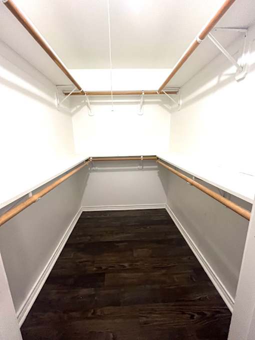 A small, neatly organized room with a bed, pillows, and a shelf.