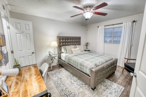 Furnished bedroom with gray upholstered bed and area rug at Le Montreaux Apartments, Austin, Texas