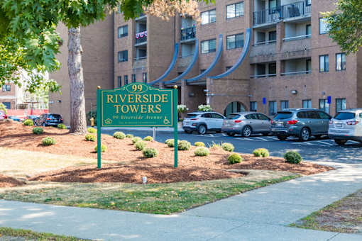 A sign for Riverside Towers stands in front of a parking lot.