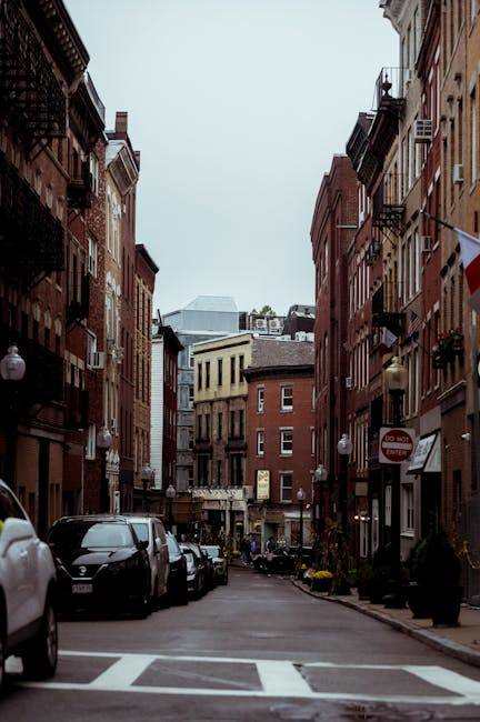 A city street with cars parked on the side and buildings on both sides.